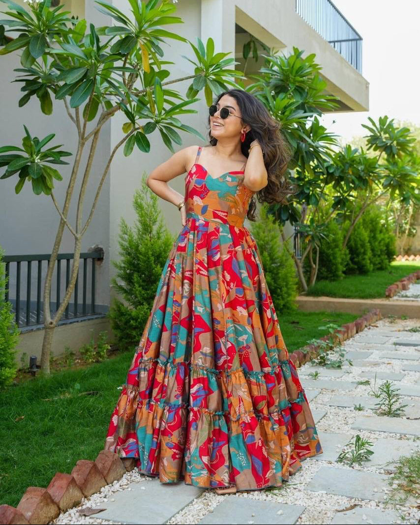 Woman in a colorful floral dress standing outdoors with greenery and a building in the background